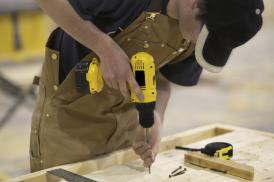 Ein Handwerker der mit einer Bohrmaschine ein Loch in Holz bohrt
